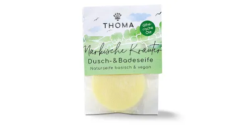 Runde, gelbliche Mini Seife in transparenter Verpackung mit grüner Aufschrift Maerkische Kraeuter, Dusch und Badeseife vegan von der Naturseifen Manufaktur Uckermark.